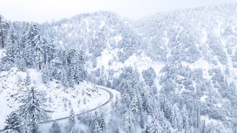 Drone view of a highway leading to Big Bear Lake after a winter storm that laid down fresh snow on the ground and pine trees.