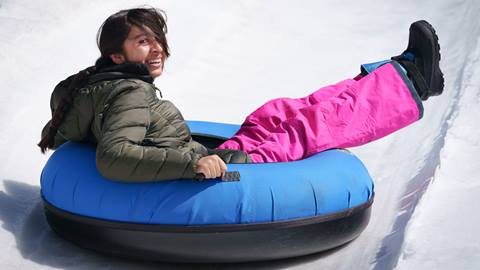 A kiddo in black jacket with pink pants riding in a snow tube while zooming down a snow lane at Snow Valley's Coyote Creek Tube Park
