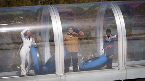 Three teens in snow gear riding the snow conveyor up the hill at Snow Valley's Coyote Creek Tube Park