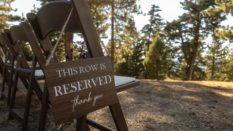 This row is reserved sign on a chair with the forest in the background ready for a wedding