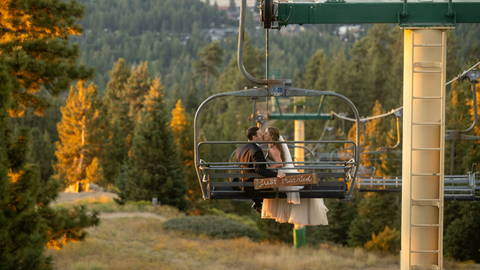 Bride and groom in the fall with orange trees and leaves in the background, taking a scenic sky chair ride at snow summit