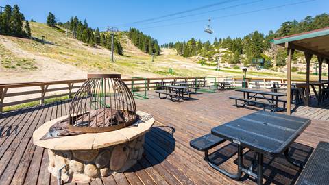 Snow Valley's sun deck with black picnic tables and a rock with metal cage fire place at Deer Meadow Grill, during the summer time when the dining venue is closed for operations.