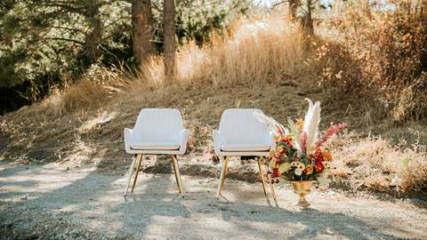 Two white chairs with some floral decor out in the forest